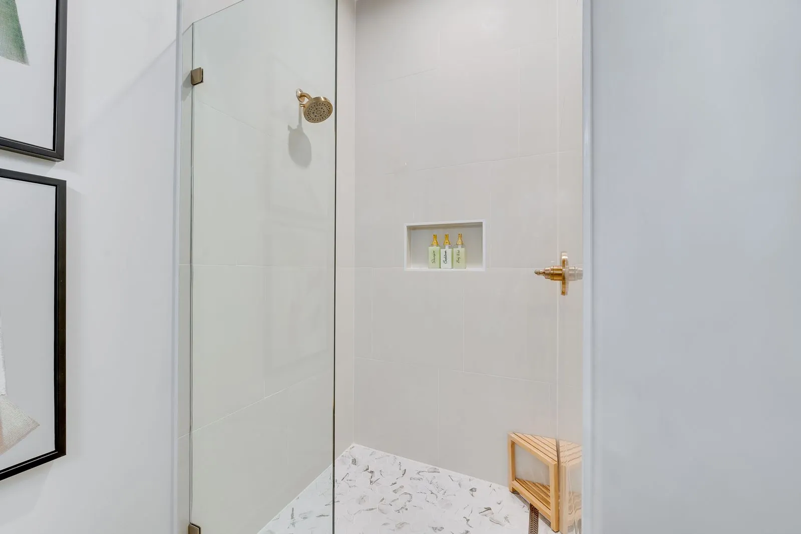 Marble shower detail at The Malibu with decorative glass jar on wood stool and gold fixtures