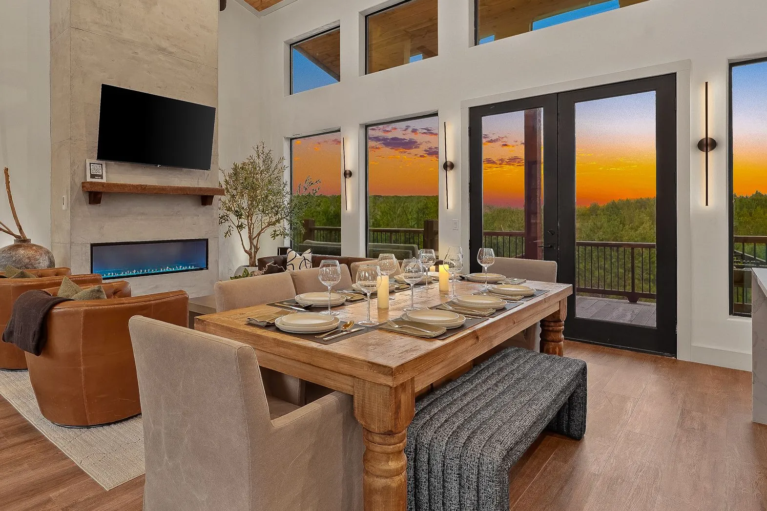 Dining and living area at The Malibu with table set for dinner, linear fireplace, and sunset views through large windows