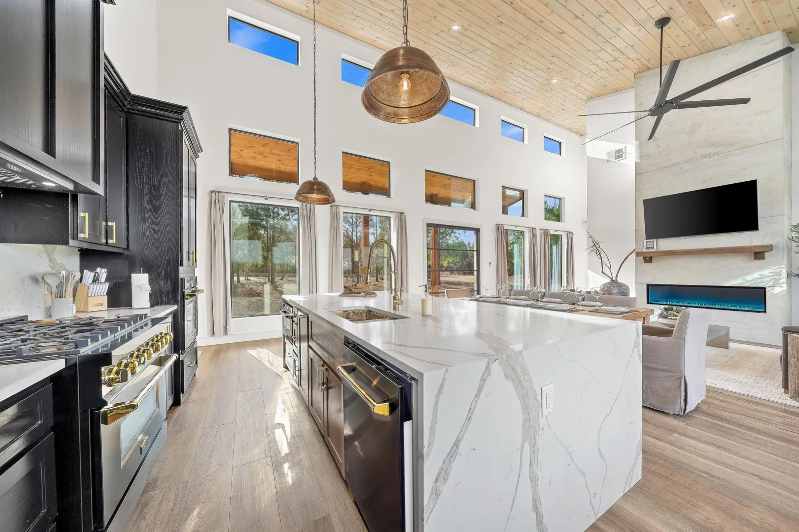 Open-concept main floor at The Malibu showing dining table, kitchen island with bar stools, and vaulted wood ceiling