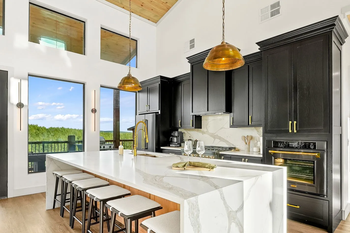 Gourmet kitchen at The Malibu with dark cabinetry, marble waterfall island, bar stools, and gold pendant lights