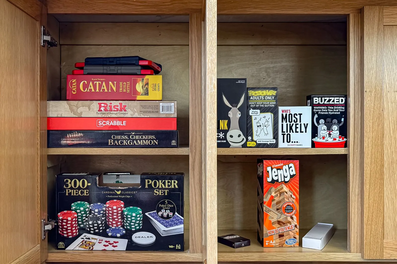 Board game collection at The Malibu including Catan, Risk, Scrabble, poker set, Jenga, and card games in wooden cabinet