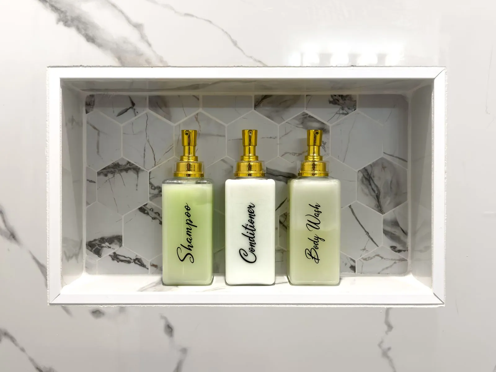 Built-in marble shower niche at The Malibu with premium shampoo, conditioner, and body wash bottles with gold caps