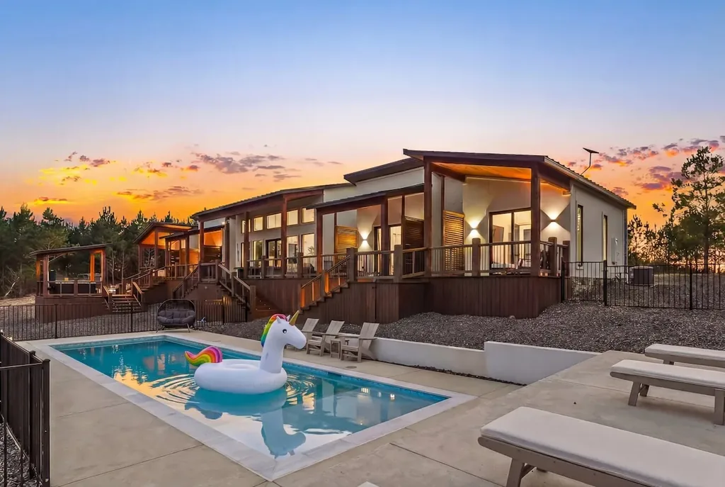 Heated pool with unicorn float, loungers, and The Malibu illuminated at sunset