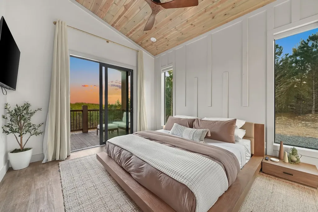 King bed beneath a vaulted wood ceiling with private balcony and sunset view