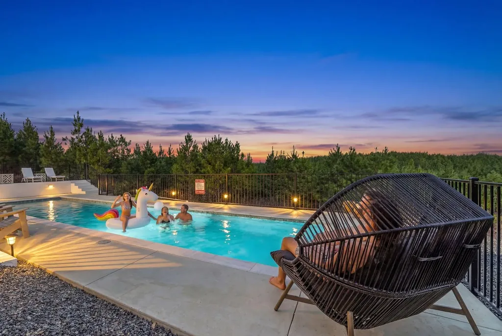 Heated pool at The Malibu at twilight with guests relaxing, wicker egg chair, and forest backdrop